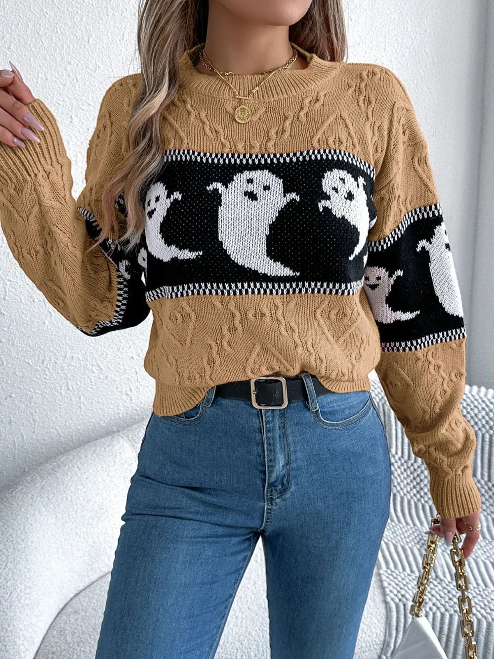 A woman wears a tan cable knit sweater with a black and white ghost pattern.