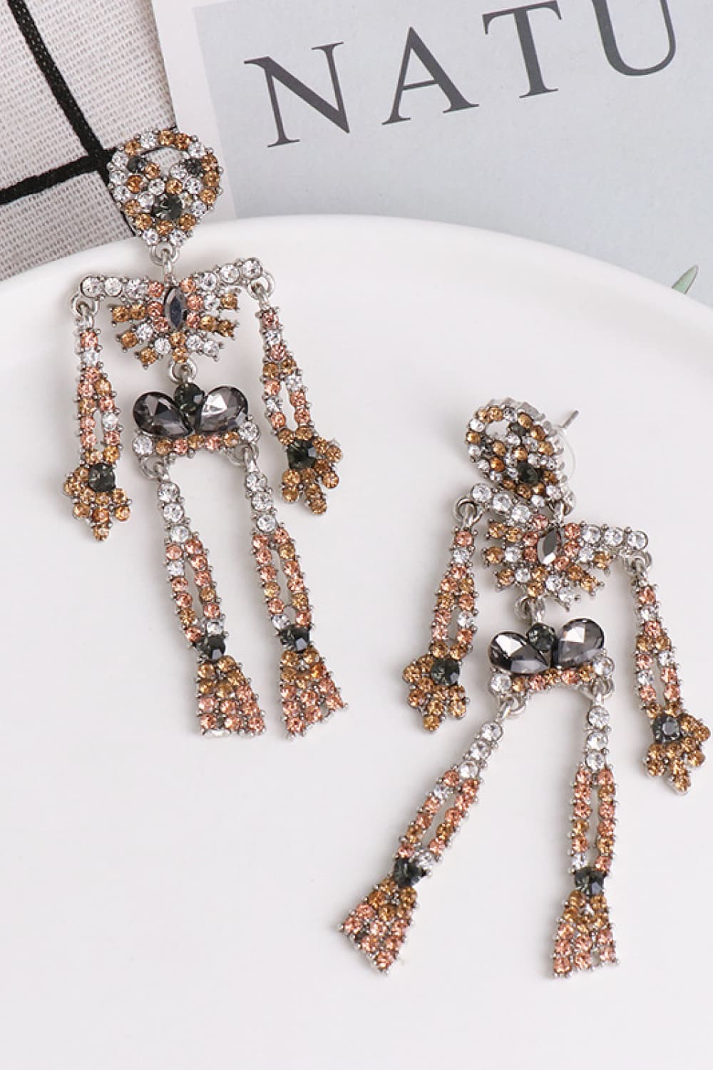 Skeleton-shaped dangle earrings adorned with clear, brown, and black glass stones.