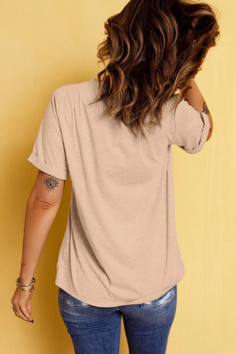 A woman from behind wearing a beige short-sleeve t-shirt and blue jeans.
