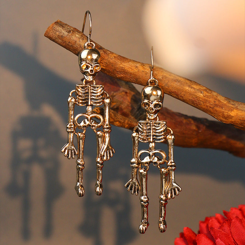 Two gold-colored skeleton alloy earrings hang from a branch.