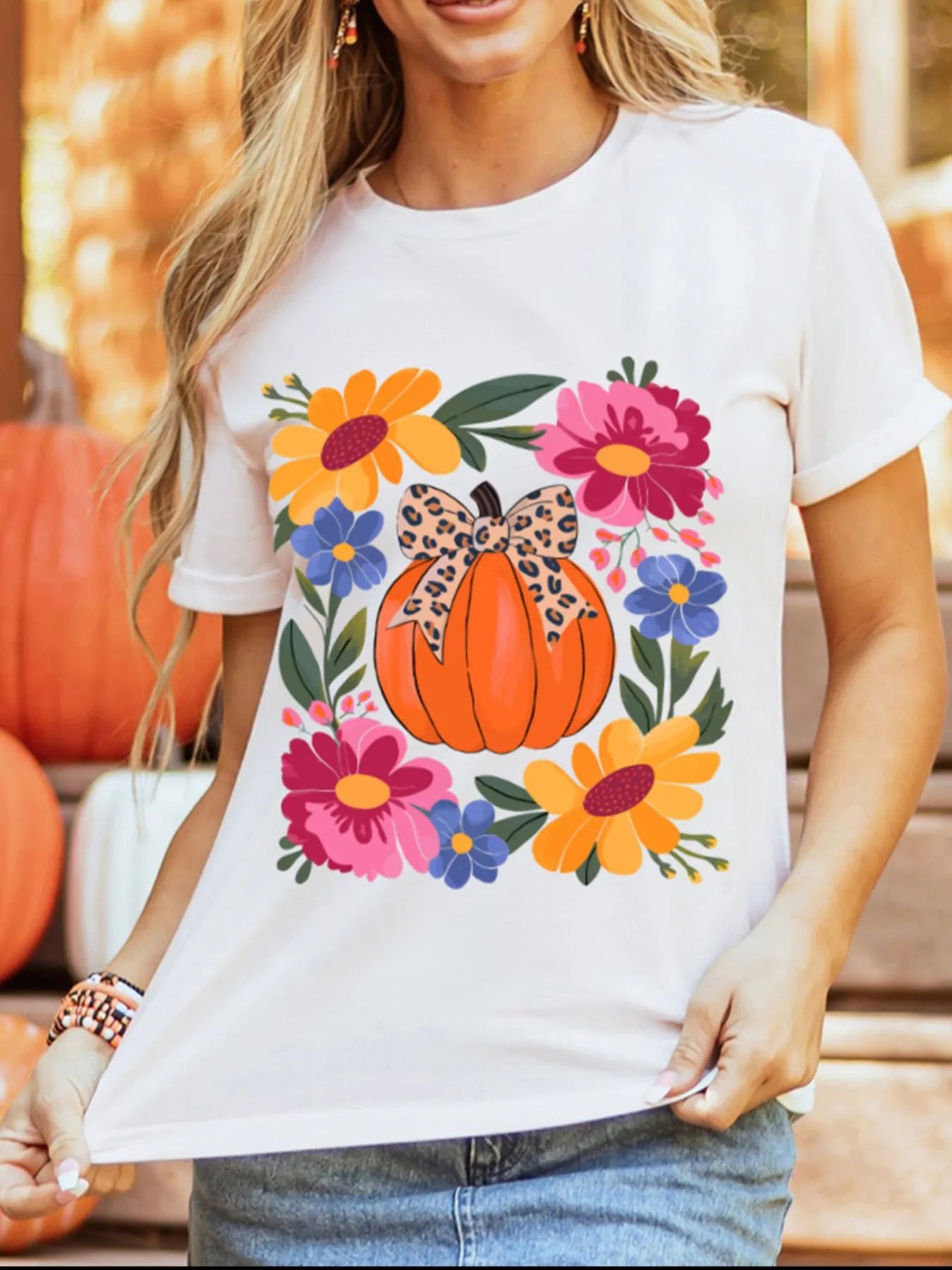 A woman wears a white t-shirt with a pumpkin and floral graphic.