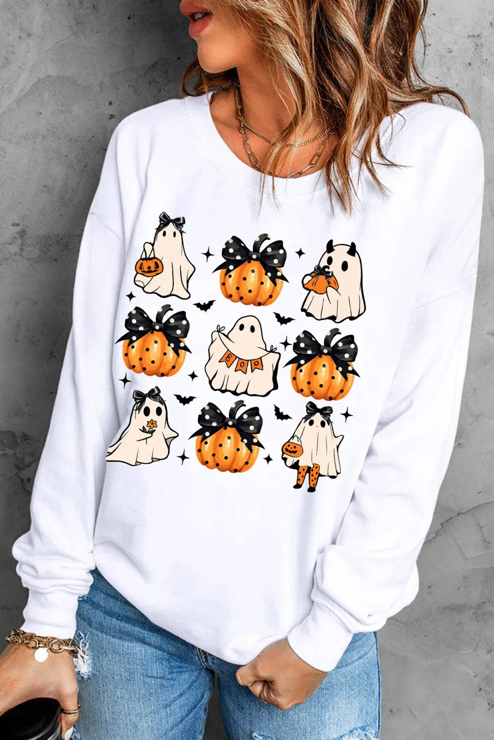 A woman wears a white long-sleeve sweatshirt with pumpkin and ghost designs.