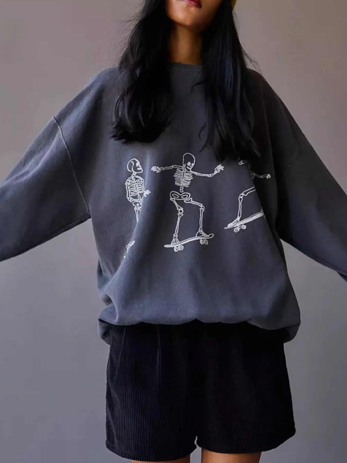 Oversized gray sweatshirt with white skeleton graphic and black corduroy shorts.