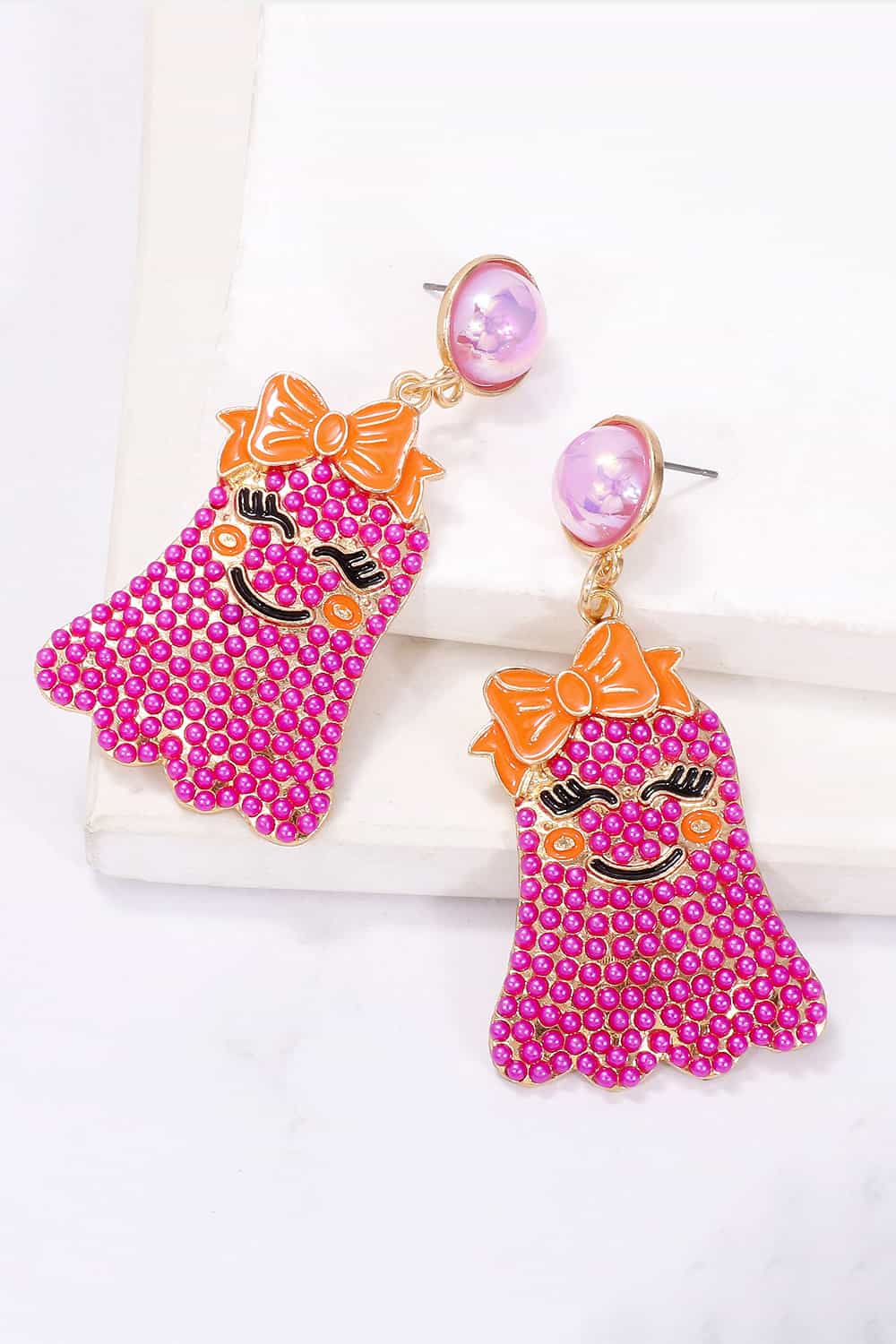 Two pink ghost-shaped earrings with orange bows and smiling faces.