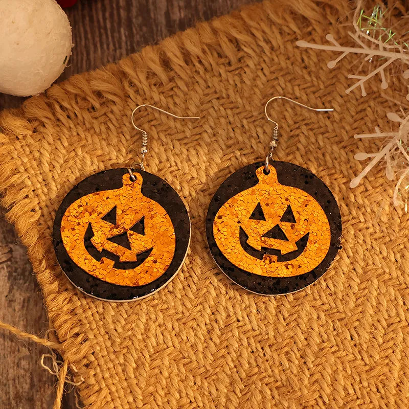 A pair of round, black and orange glittery pumpkin earrings on a burlap surface.