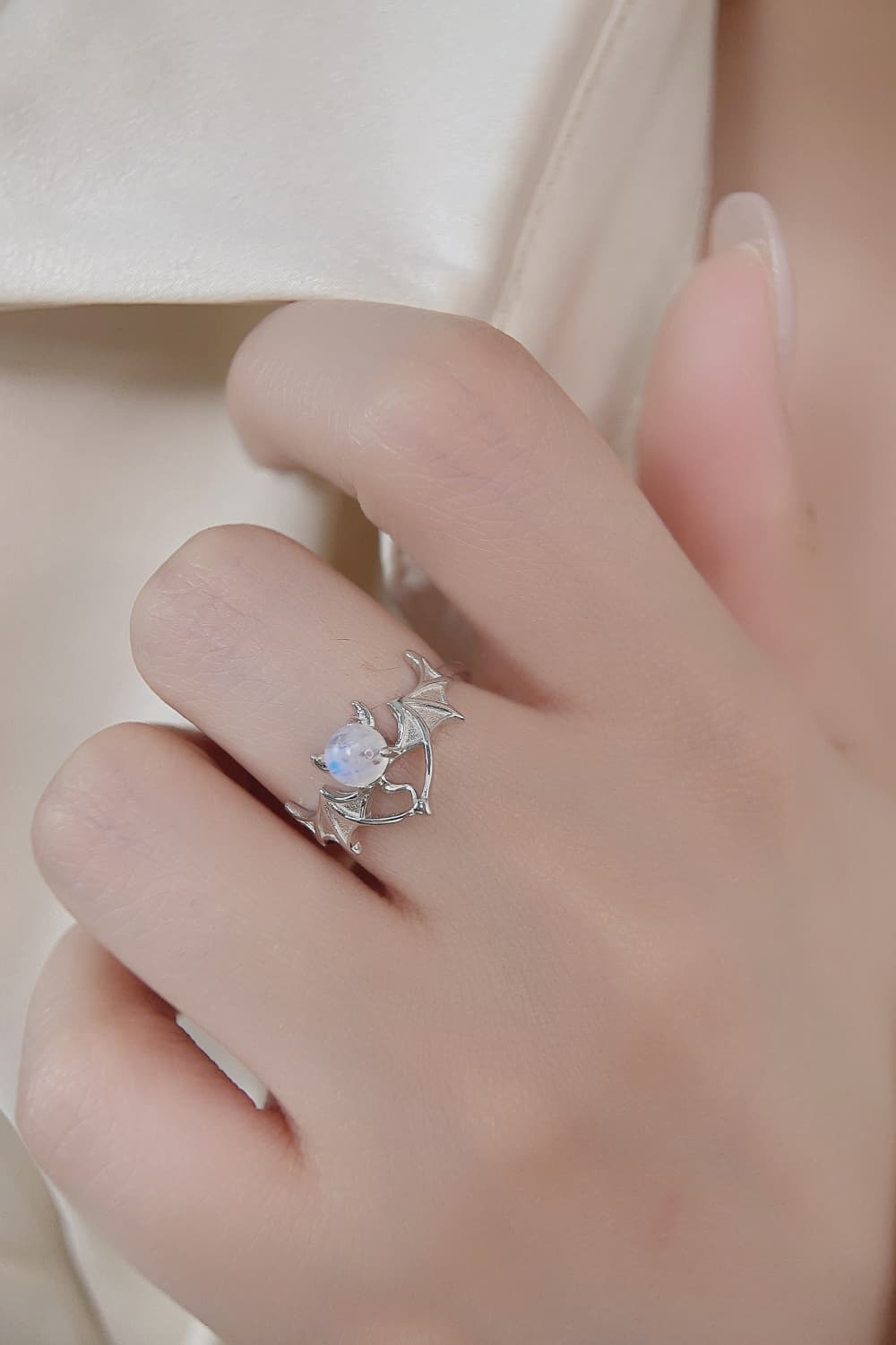 A silver bat ring with a moonstone gem is worn on a finger.