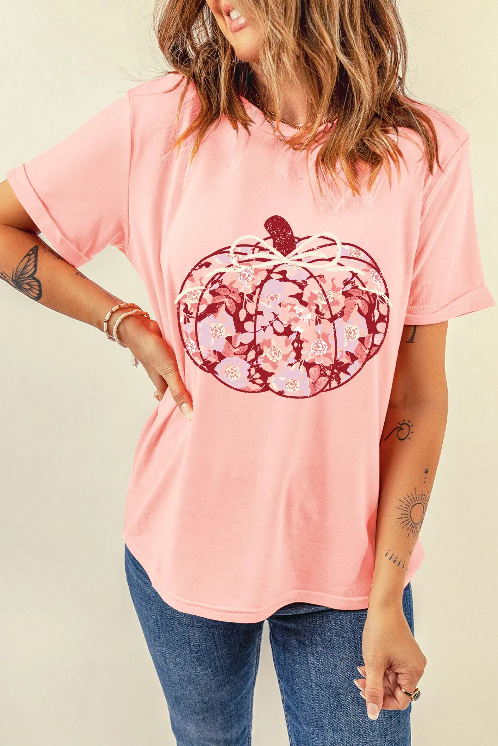 A woman wears a pink t-shirt with a floral pumpkin graphic and blue jeans.