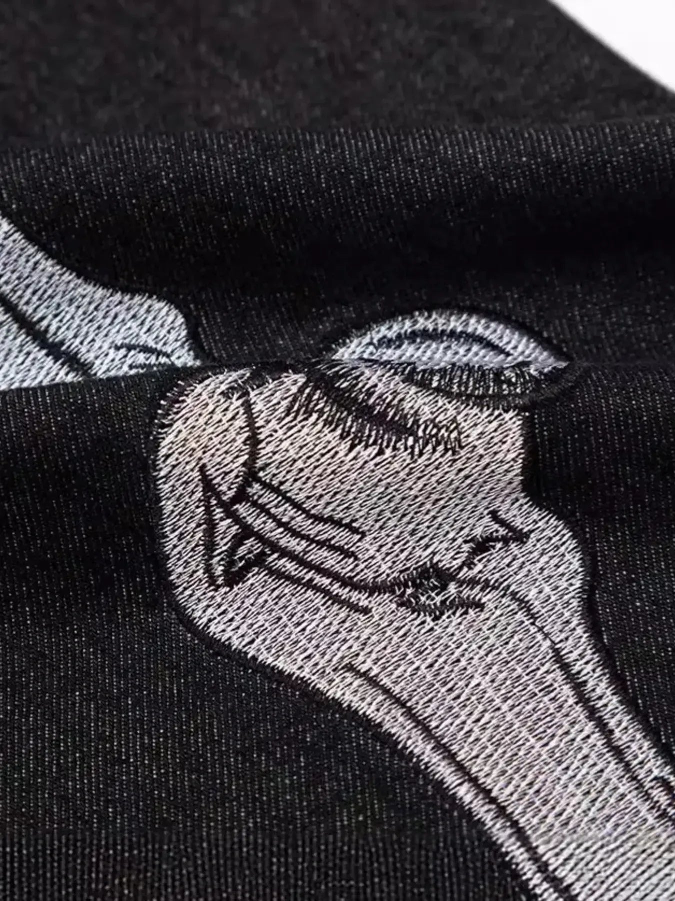 Close-up of black jeans with white skeleton embroidery on the thigh.
