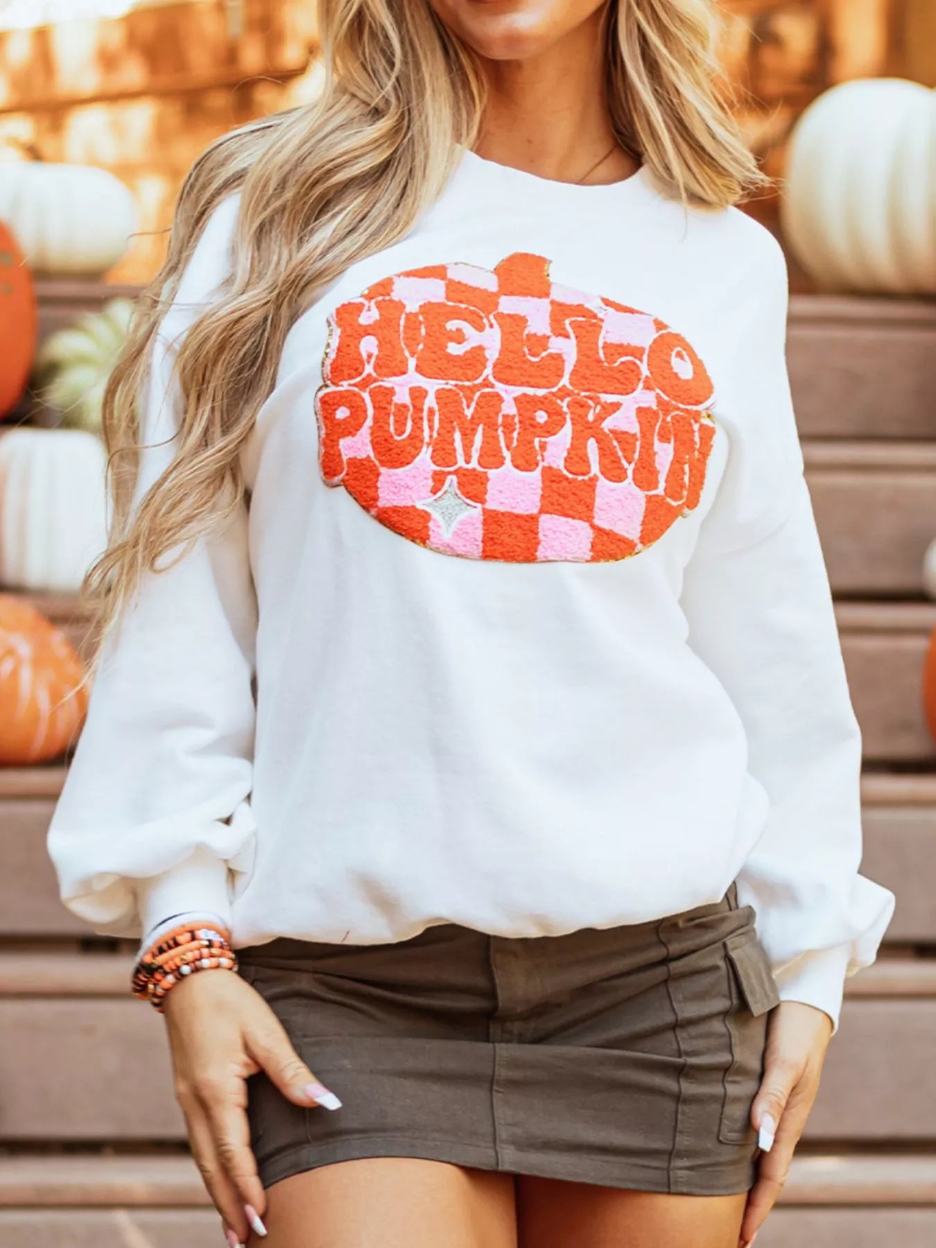 A woman wears a white long-sleeve sweatshirt with a "Hello Pumpkin" patch.