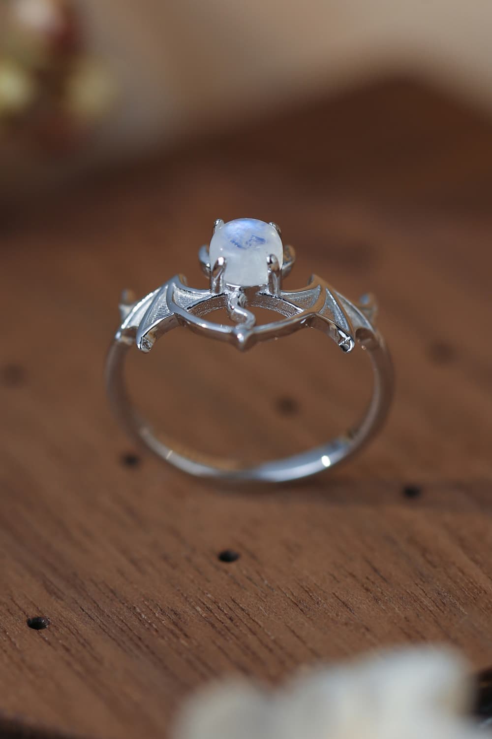 Sterling silver bat ring with a moonstone center on a wooden surface.