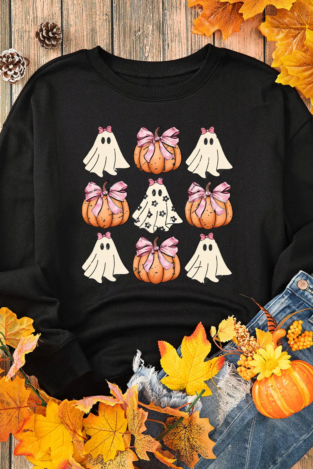 Black sweatshirt with a grid of pumpkins and ghosts, surrounded by autumn leaves.