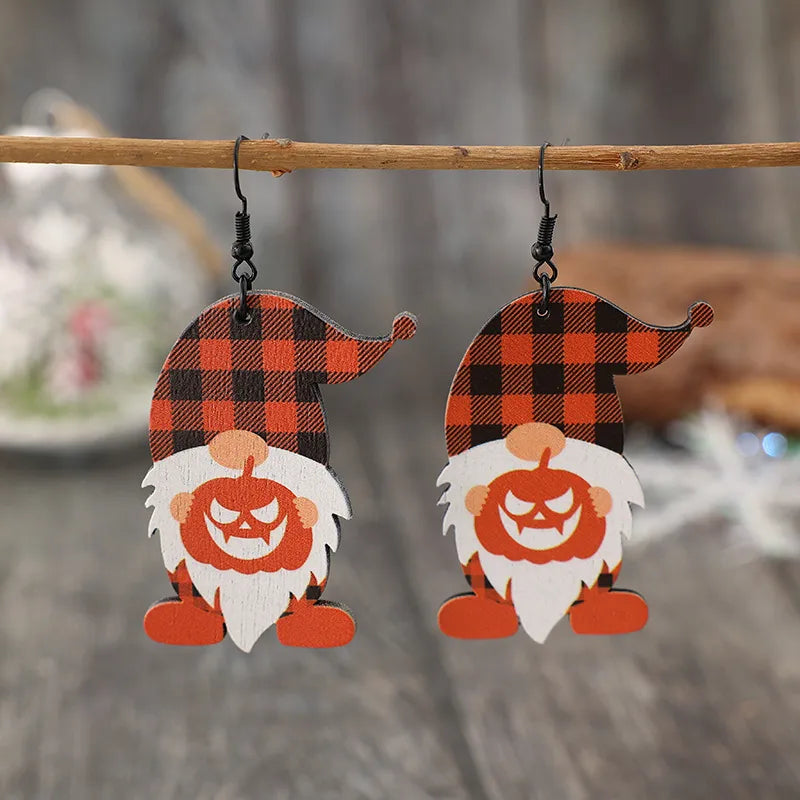Two wooden dwarf earrings with plaid hats and pumpkin faces hang from a branch.