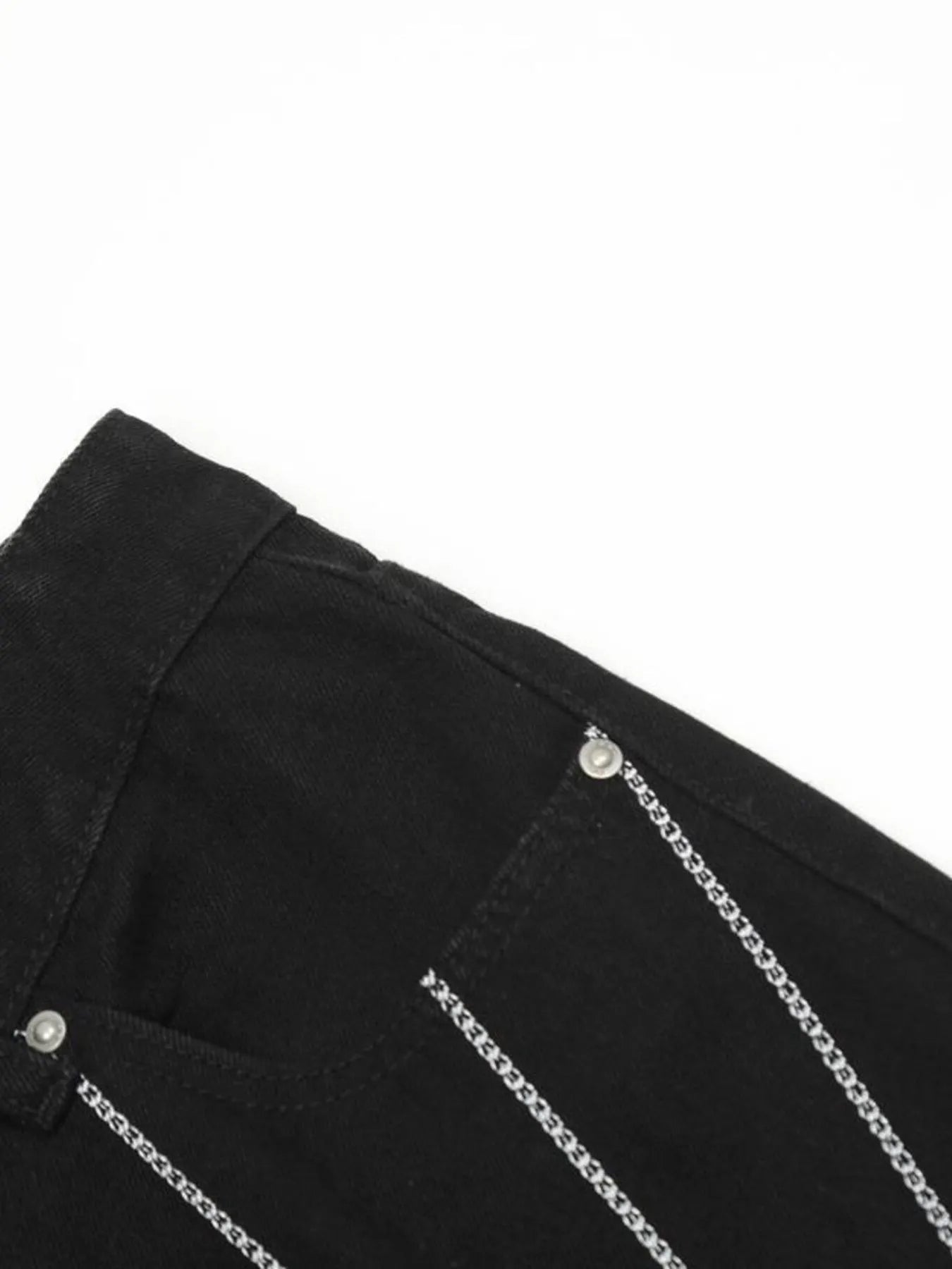 Close-up of black jeans with silver chain details and a front pocket.