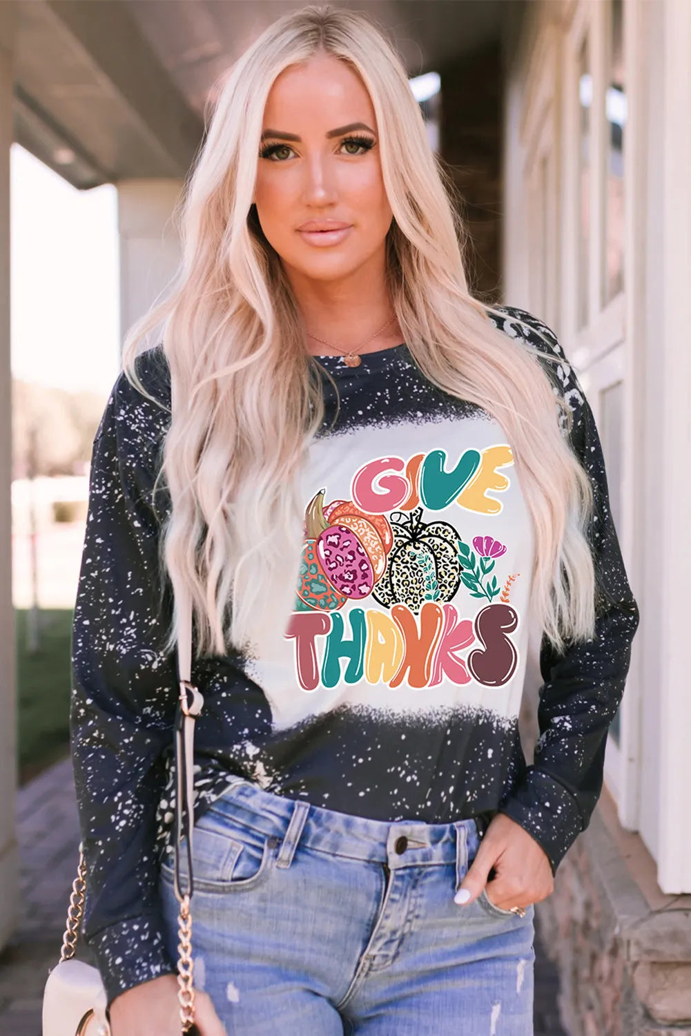 A woman models a black and white bleached long-sleeve t-shirt with a colorful "Give Thanks" pumpkin graphic.