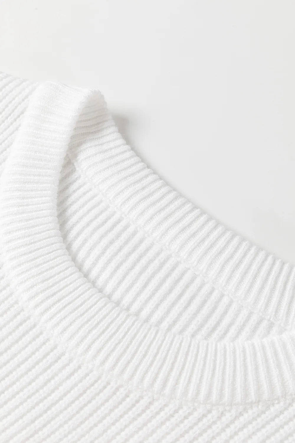 Close-up of a white ribbed knit sweater with a round neck.