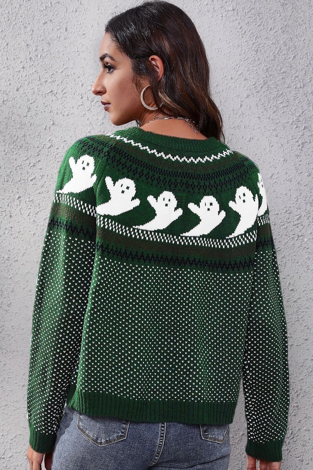 A woman models a green long-sleeve sweater with a white ghost pattern.