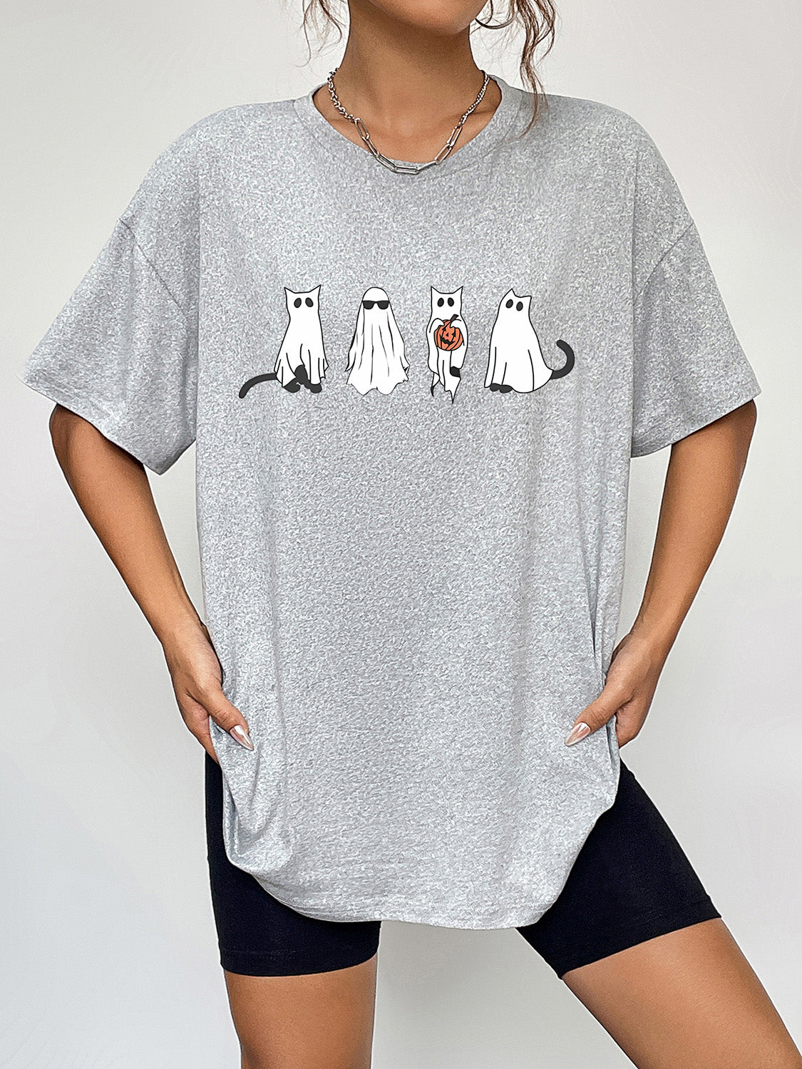 Gray short-sleeve t-shirt with a ghost cat graphic, worn by a person in black shorts.
