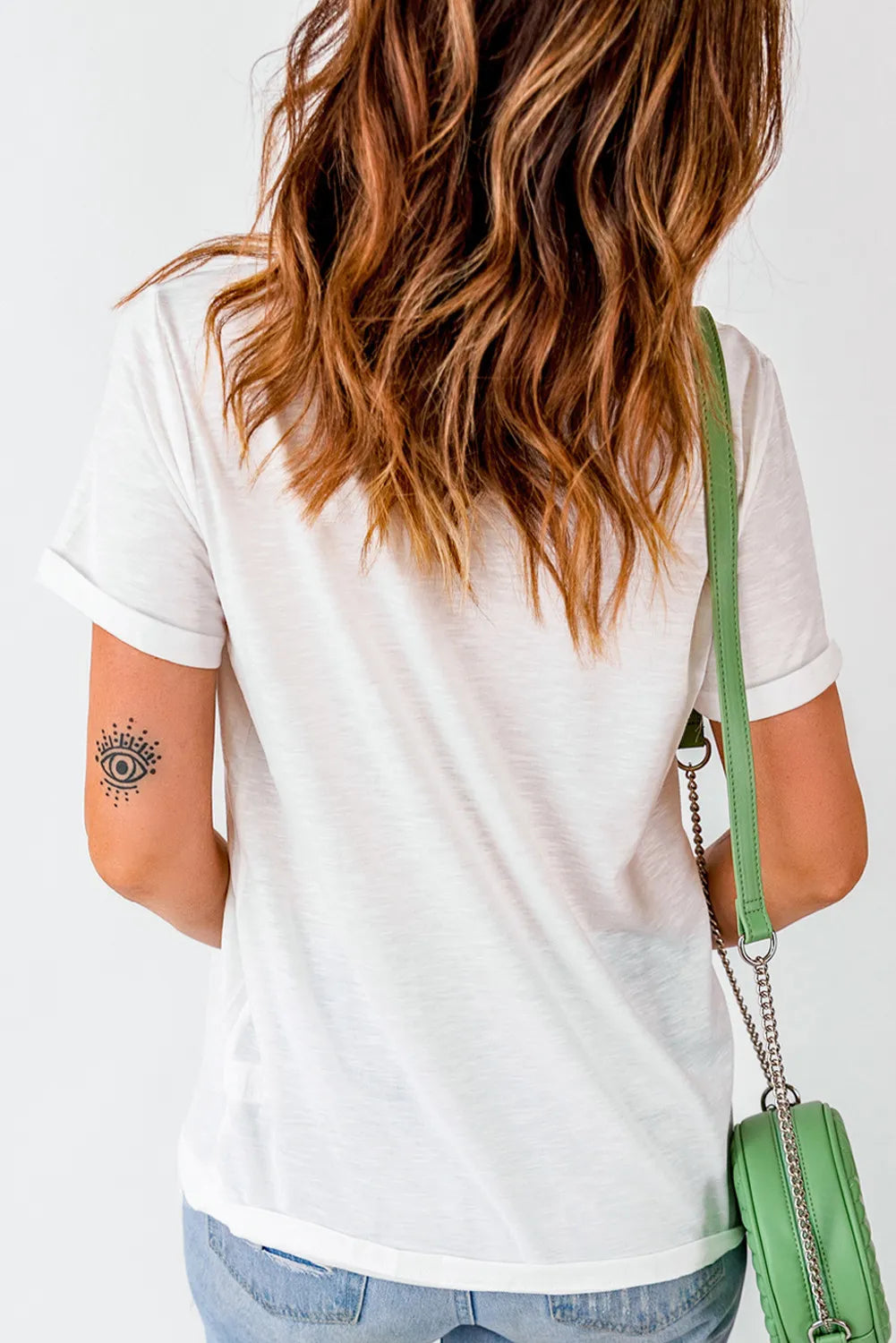 A woman from behind wears a white short-sleeve t-shirt and carries a green purse.