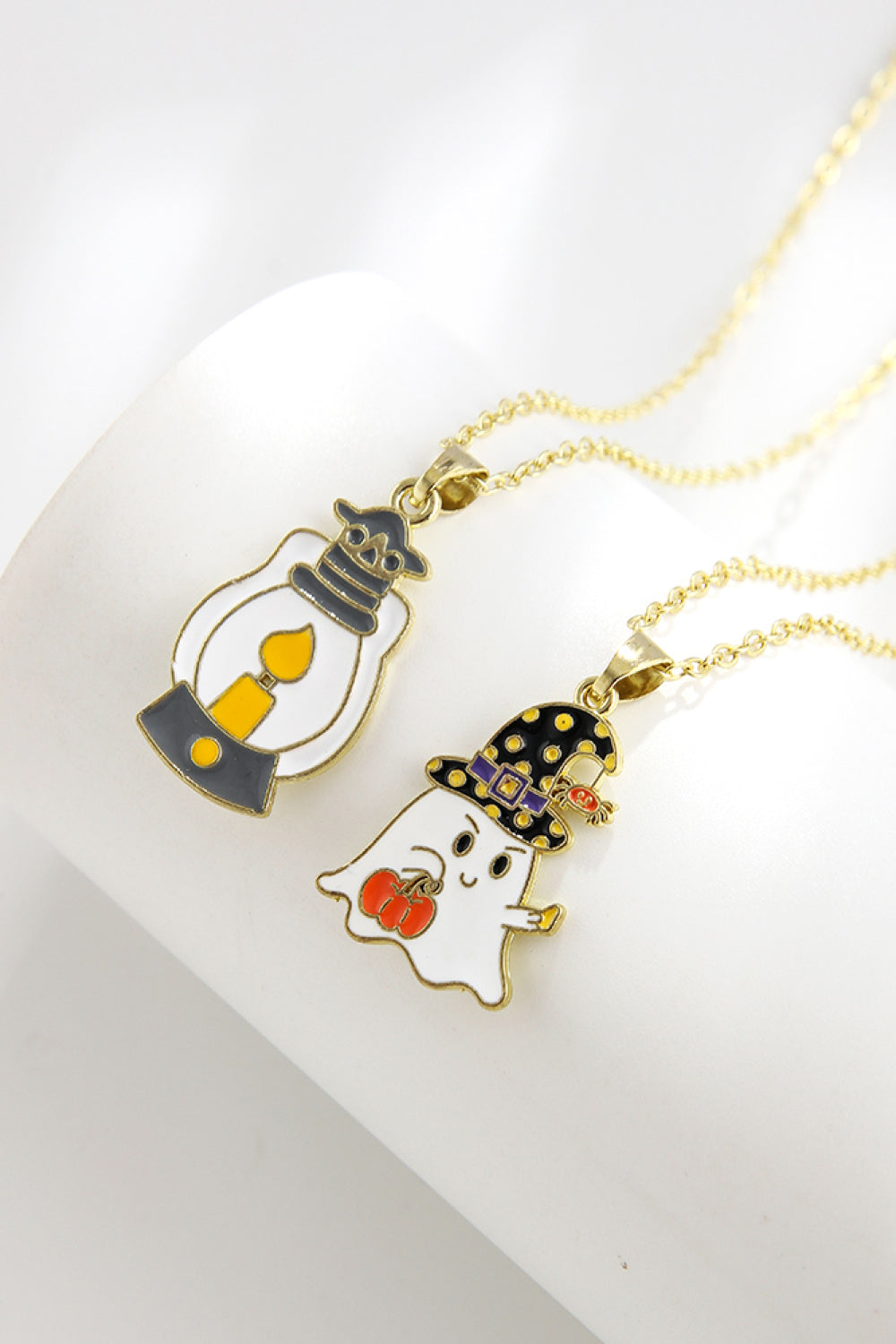 Two Halloween-themed necklaces, one with a lantern and one with a ghost, on a white surface.