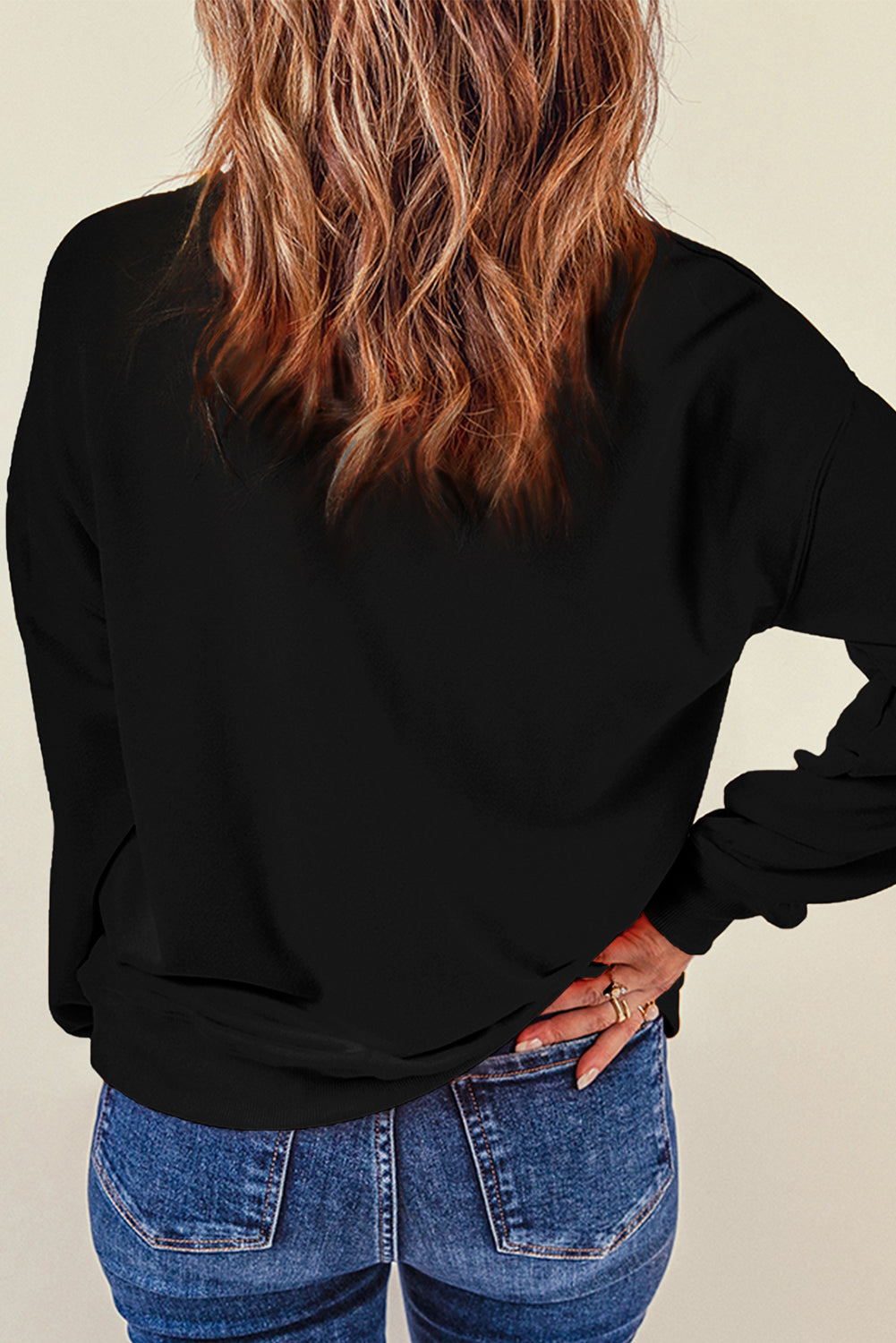 A woman from behind wears a black dropped shoulder sweatshirt and blue jeans.