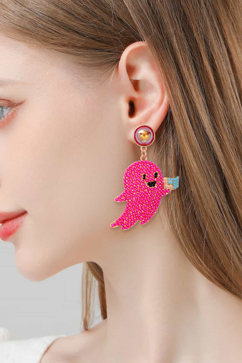 A woman wears a pink ghost-shaped dangle earring with a synthetic pearl stud.