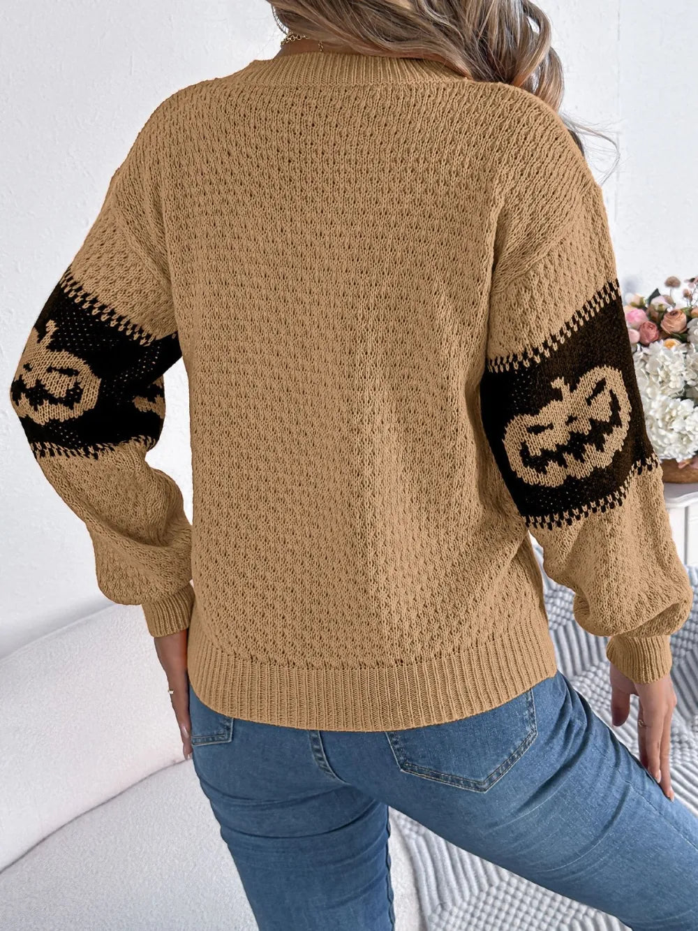 A woman from behind wears a tan pumpkin round neck long sleeve sweater and jeans.