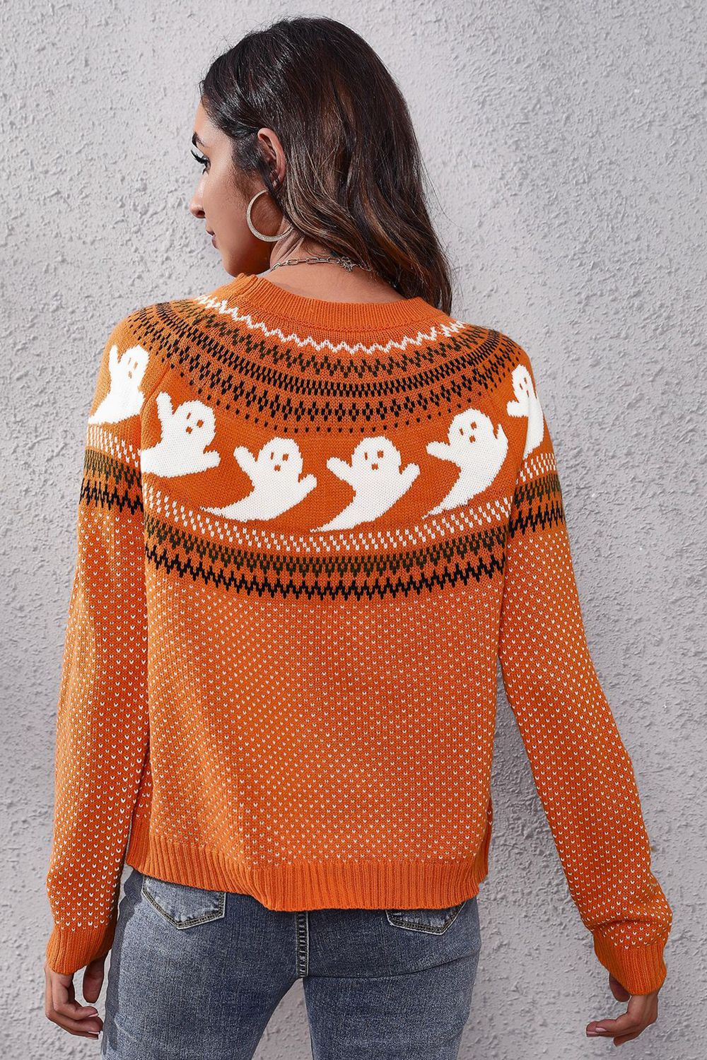 A woman from behind wears an orange round neck long sleeve sweater with a ghost pattern.