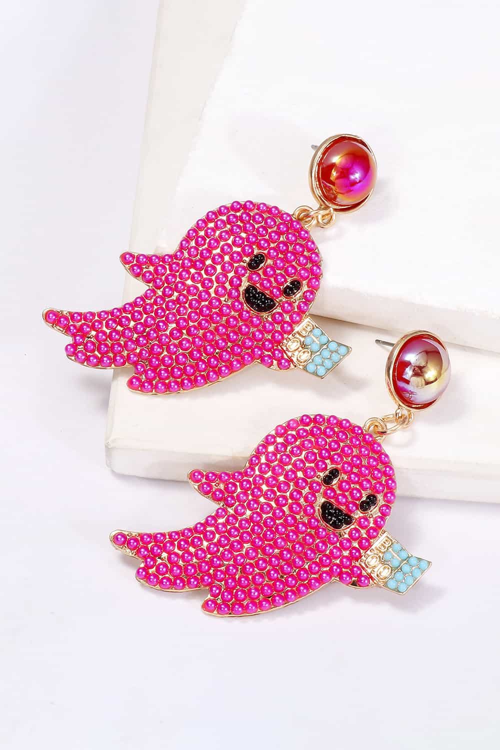 Pink ghost-shaped dangle earrings with synthetic pearls and a small blue book.