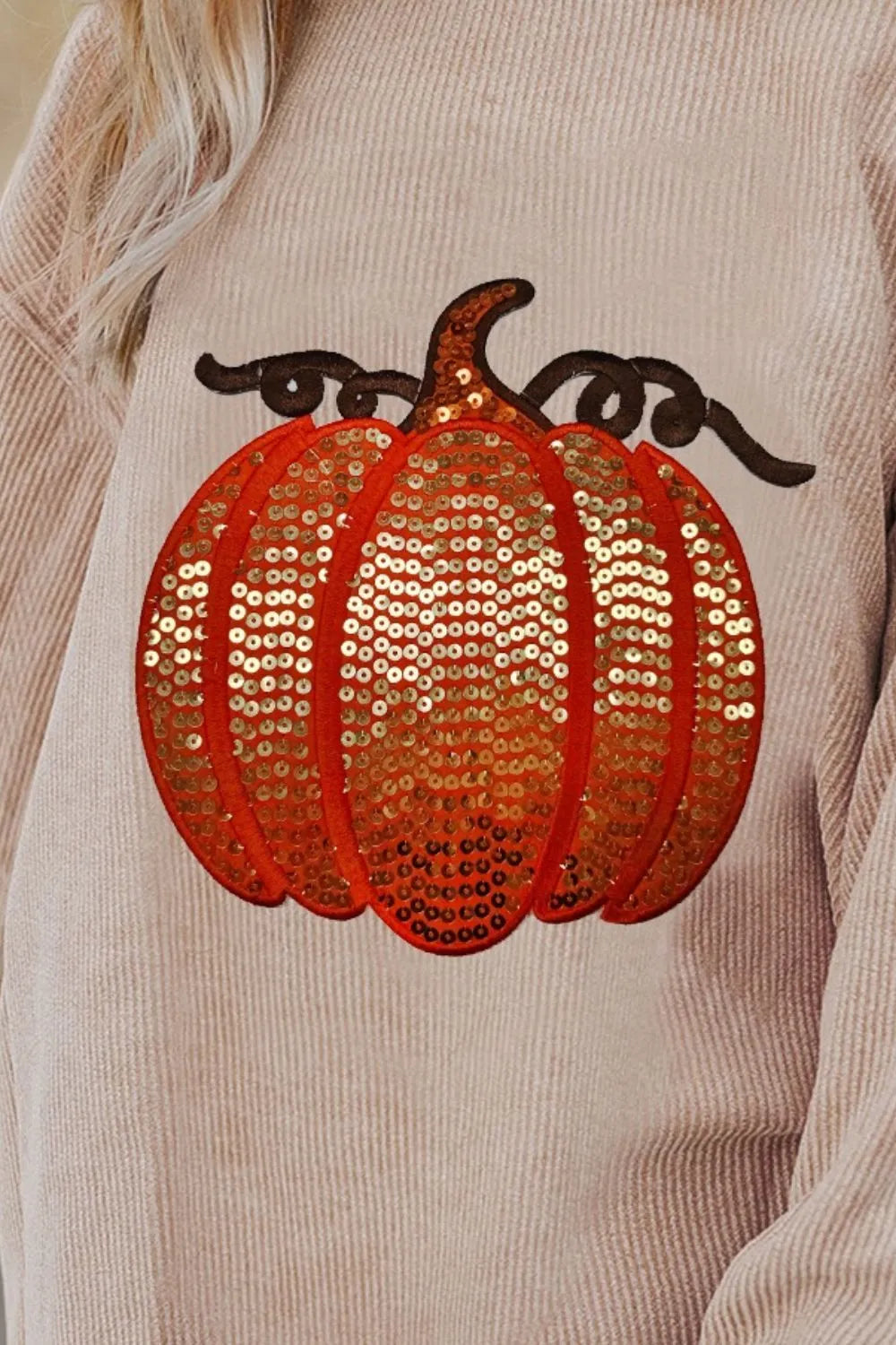 A beige long-sleeve sweatshirt features a large, orange sequin pumpkin design.