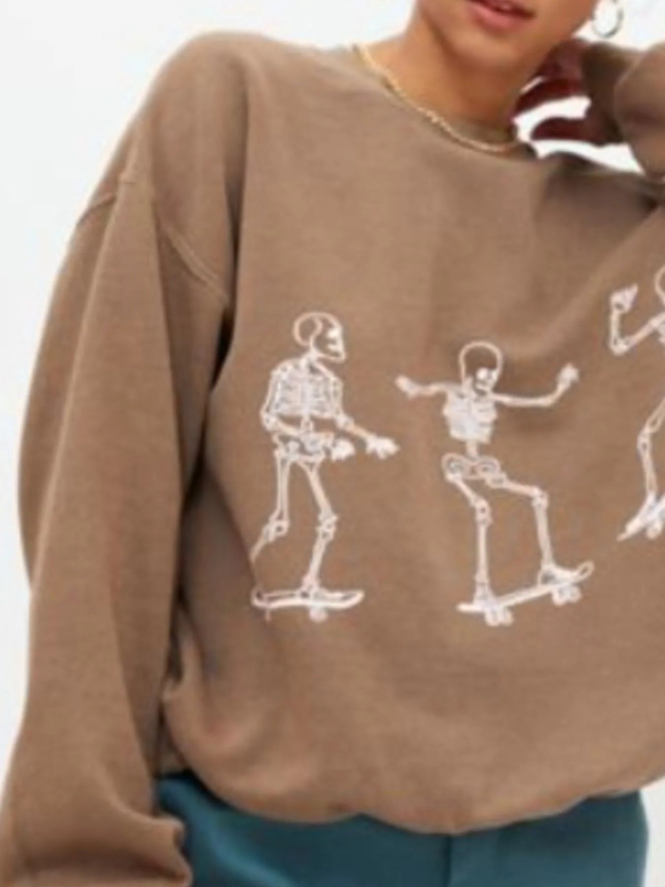 An oversized brown sweatshirt with white skeleton graphics skateboarding.