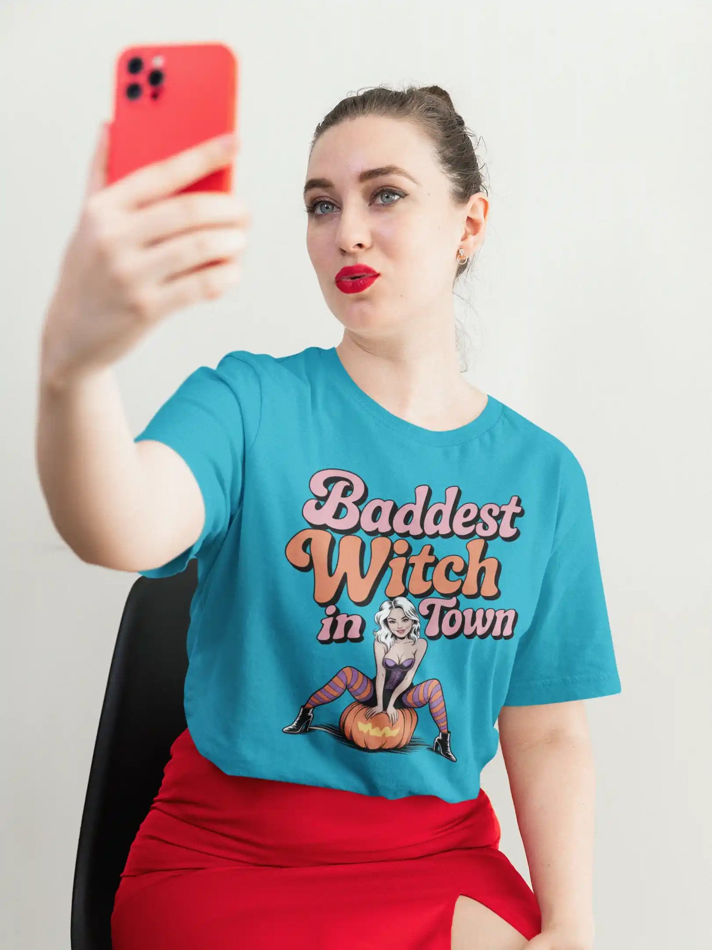A woman in a blue t-shirt with "Baddest Witch in Town" graphic takes a selfie.