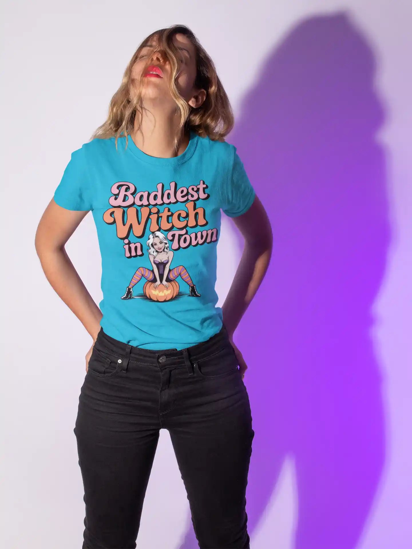 A woman wears a blue t-shirt with "Baddest Witch in Town" and a witch on a pumpkin.