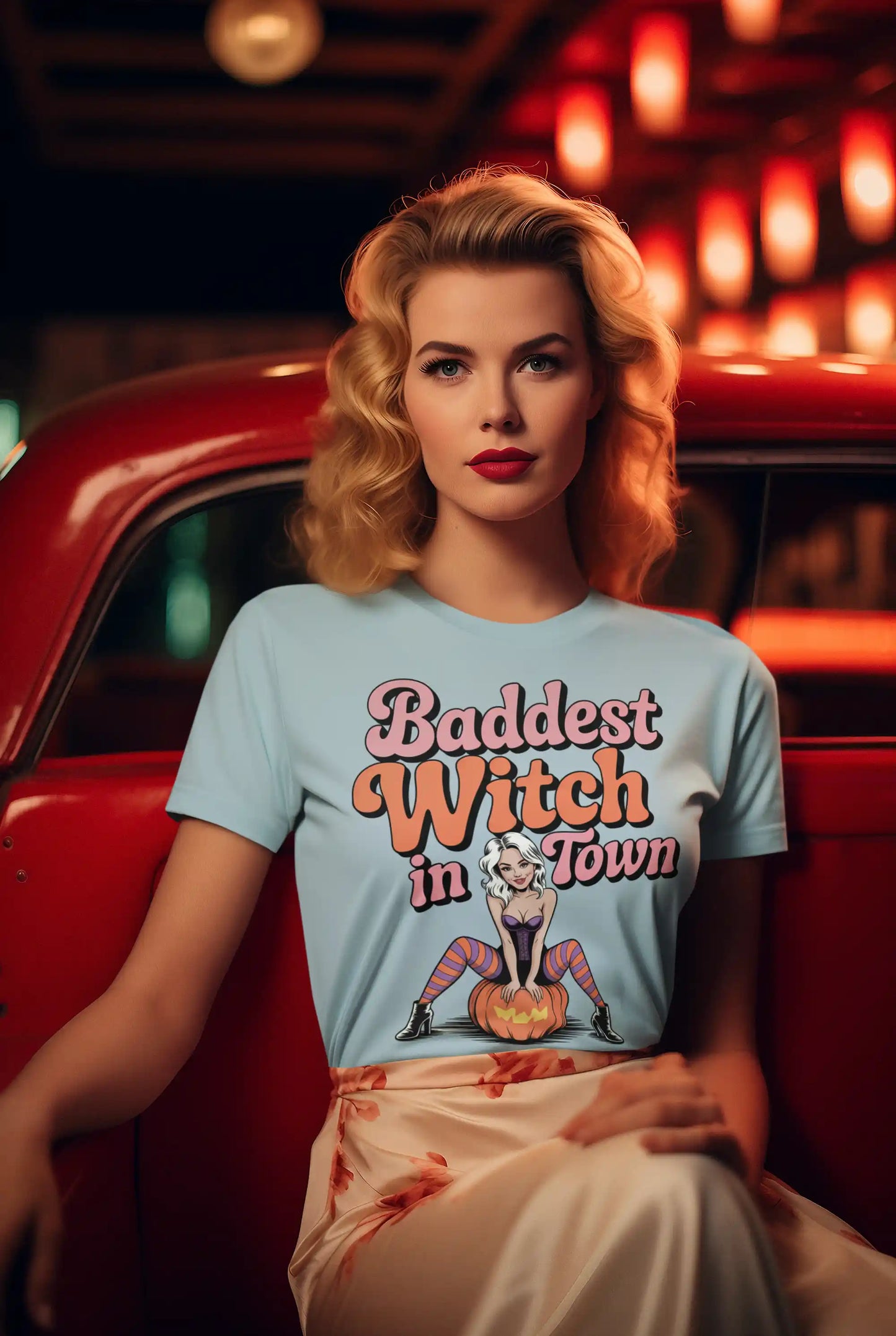 A woman in a light blue t-shirt that says "Baddest Witch in Town" sits in a red car.