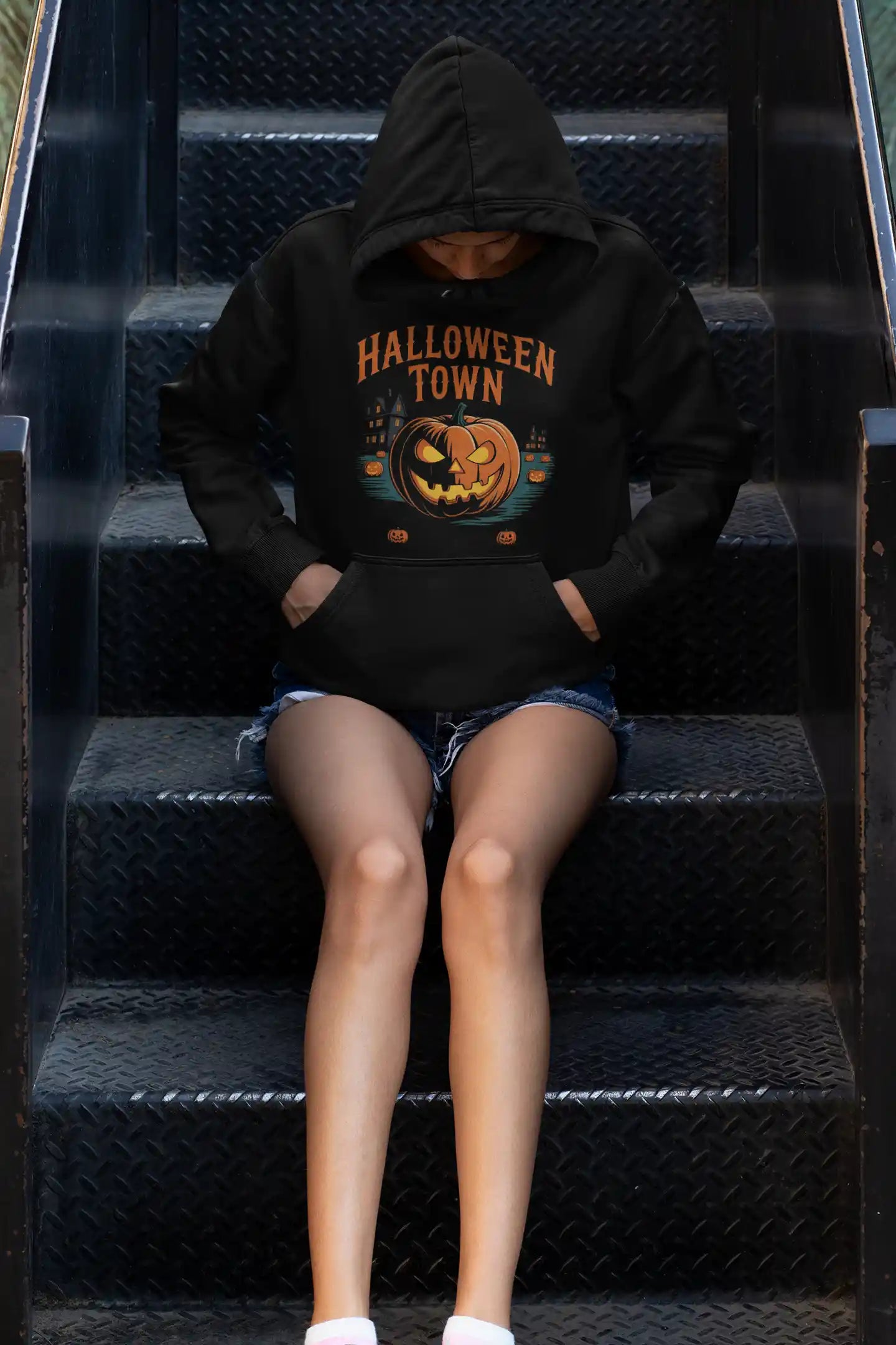 Black Halloween Town hoodie with a vintage pumpkin graphic, worn by a person sitting on stairs.
