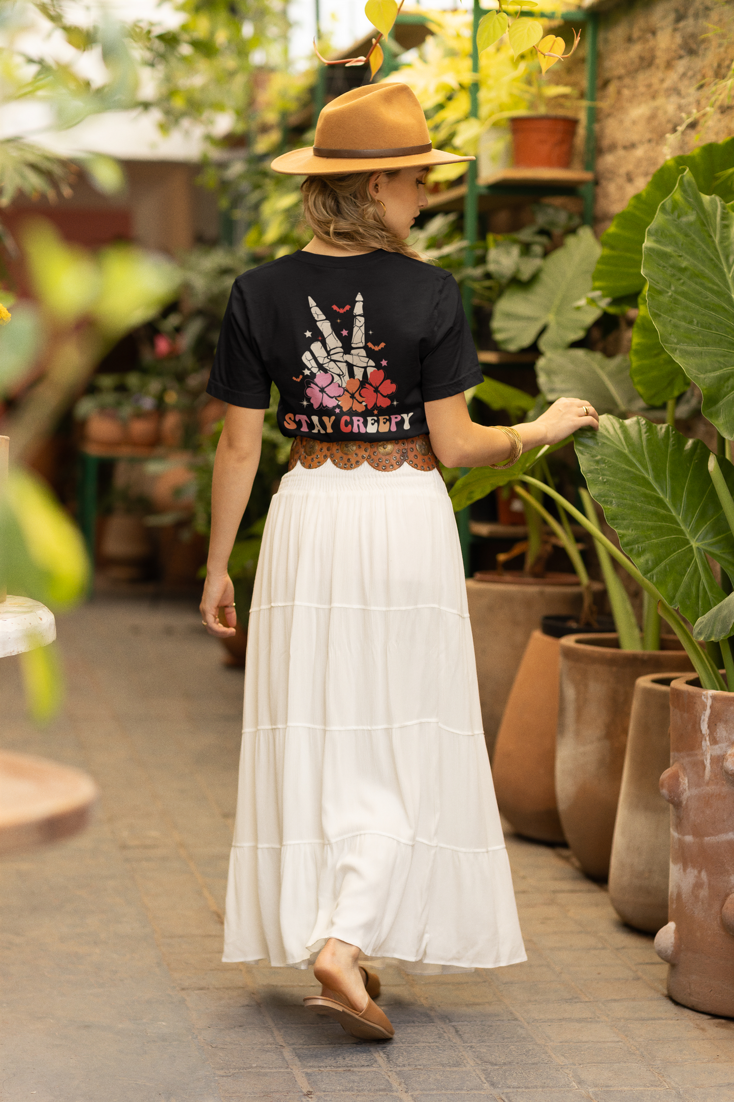 A woman from behind wears a black t-shirt with a skeleton peace sign and flowers.