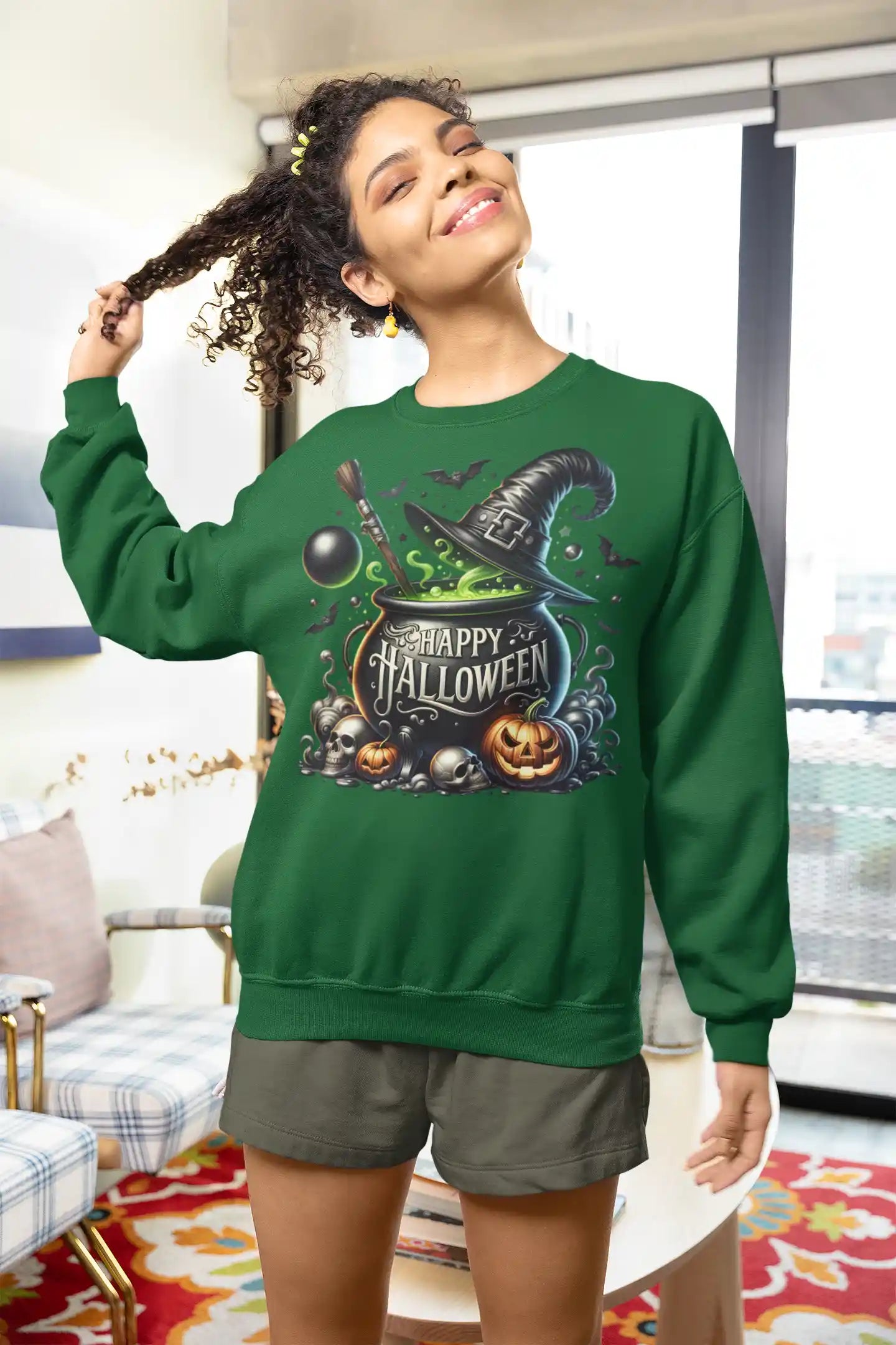 A woman in a green sweatshirt with a Halloween graphic smiles while pulling her curly hair.