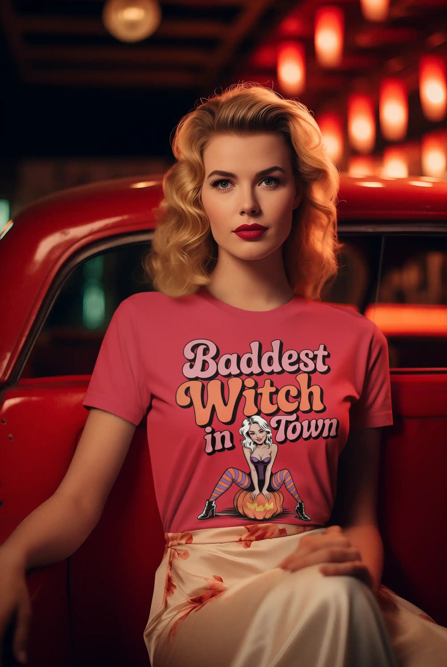 A woman in a pink "Baddest Witch in Town" t-shirt sits in a red car.