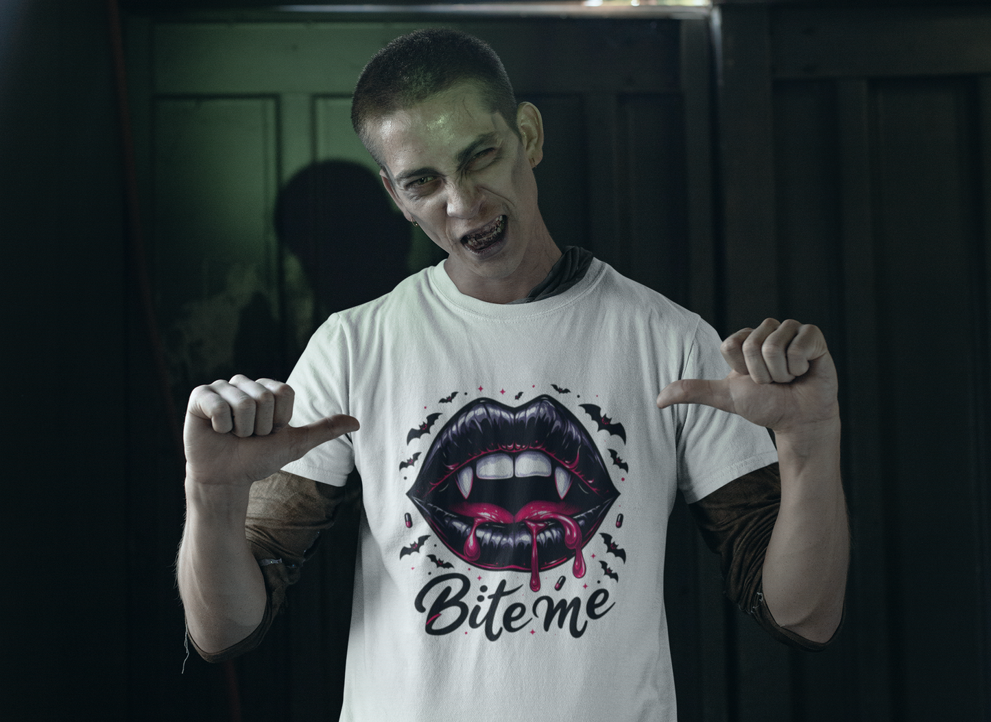 A man in vampire makeup points to a white t-shirt with a "Bite Me" design.