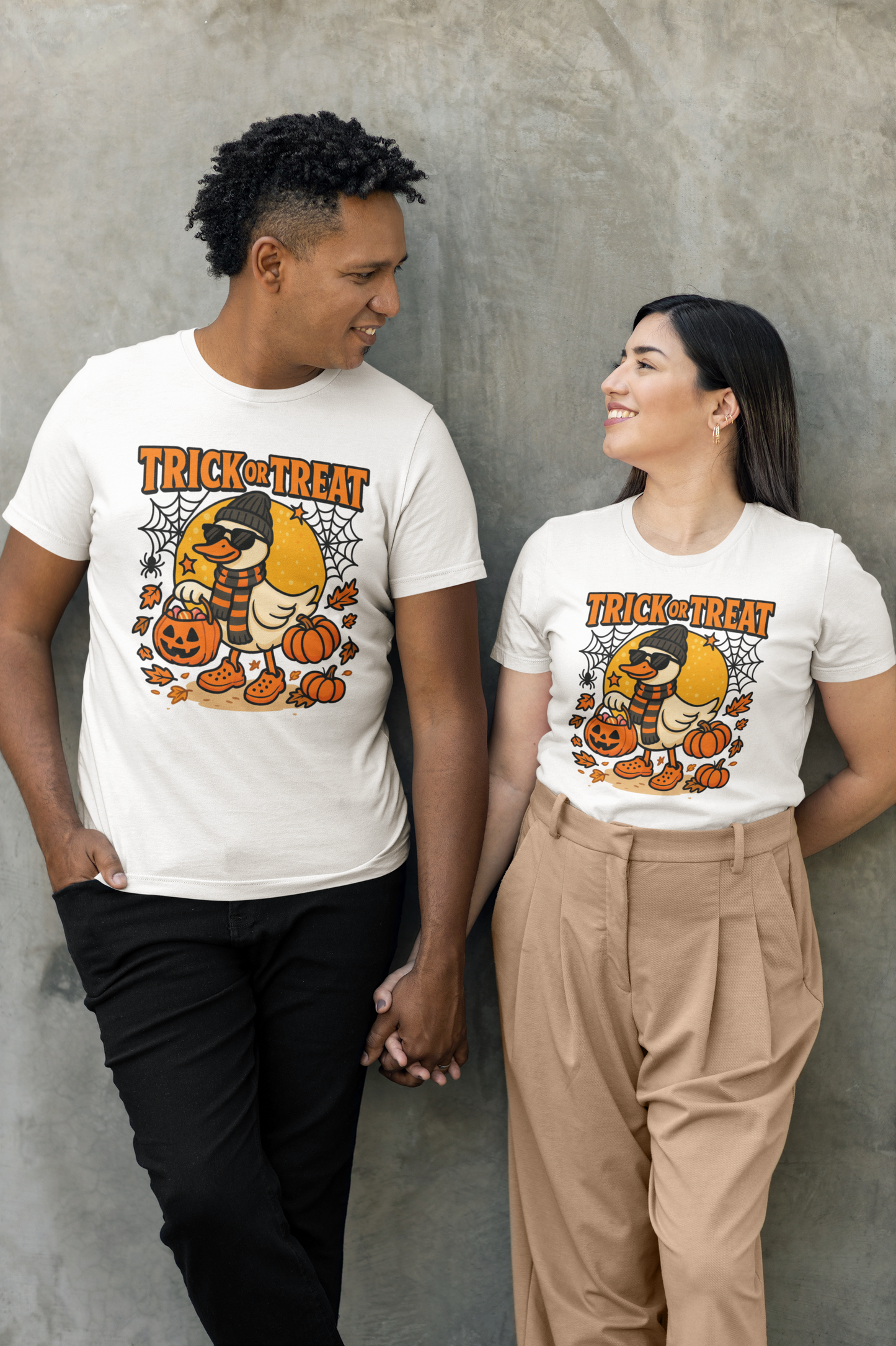 Two people wear white "Trick or Treat" t-shirts with a duck, pumpkins, and spiderwebs.