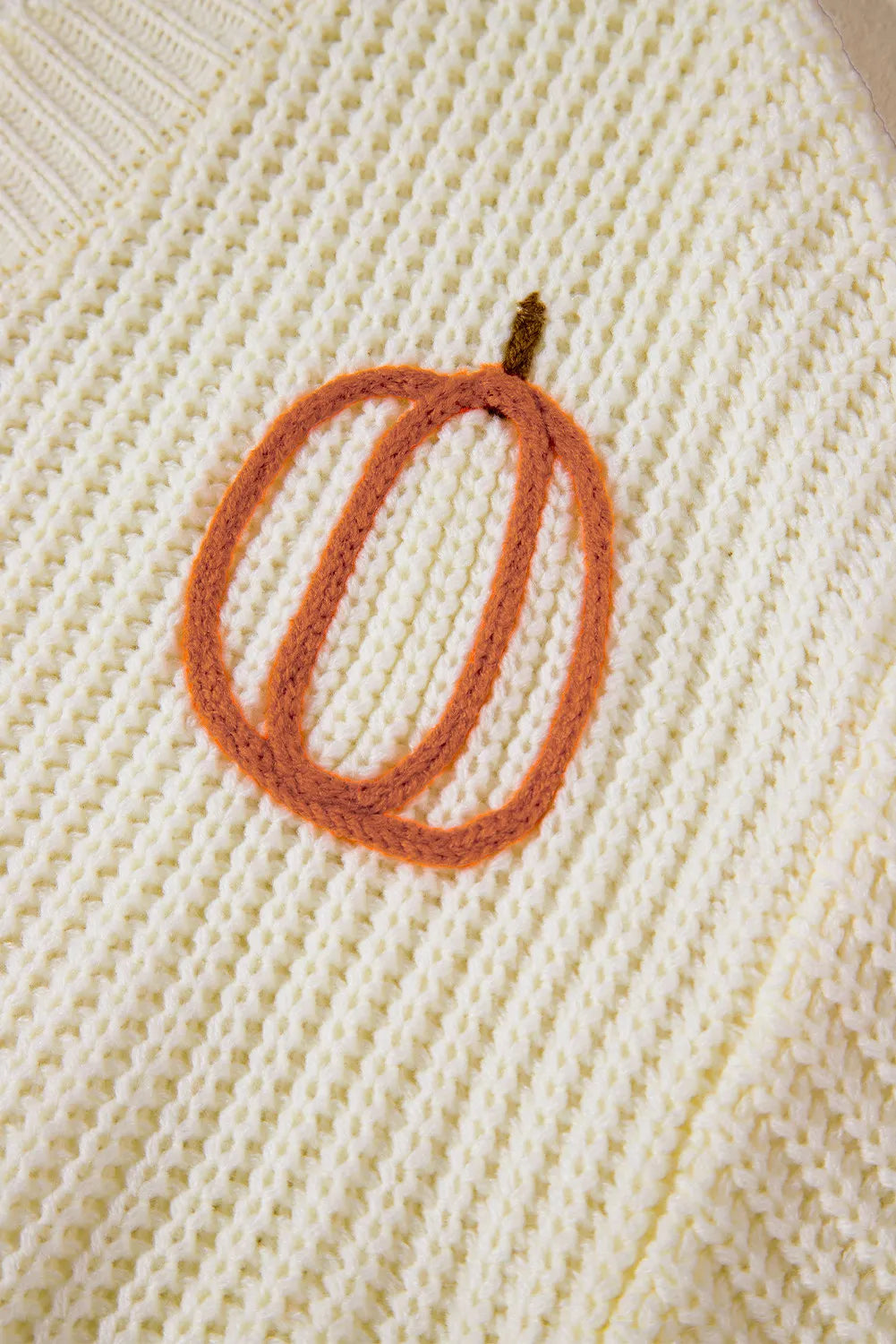 Close-up of a cream knit sweater with an orange pumpkin outline.