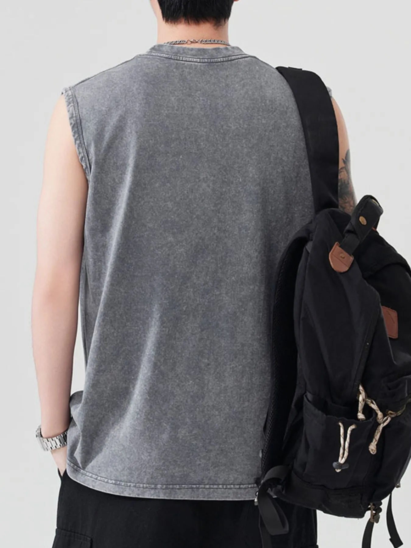 Back view of a man wearing a gray, acid-washed tank top and a black backpack.