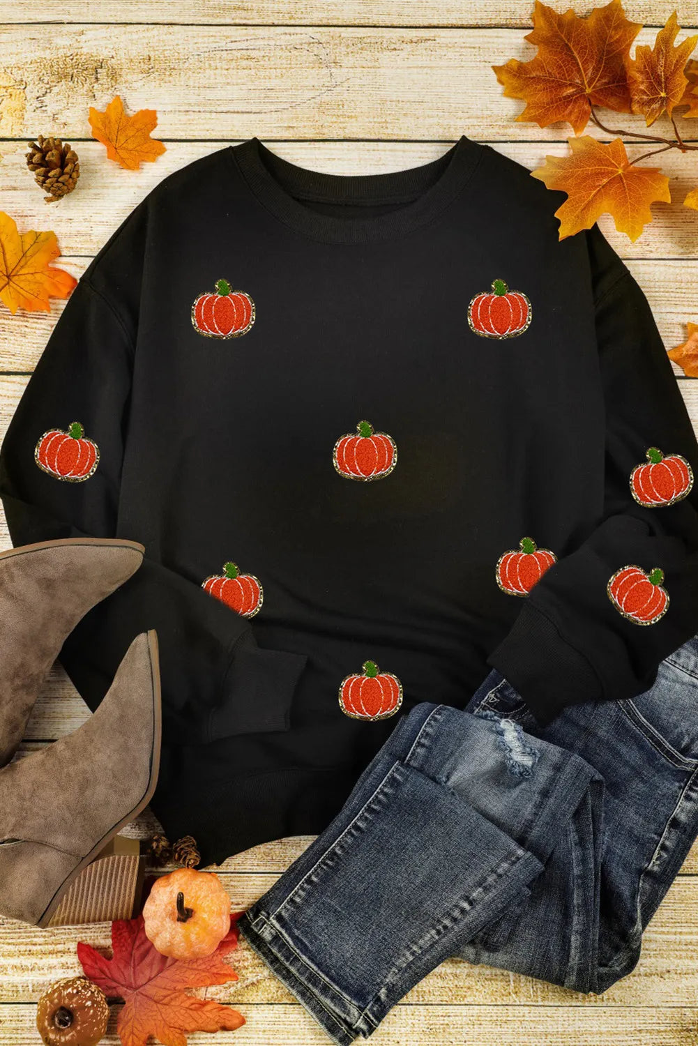 Black long-sleeve sweatshirt with sequin pumpkin appliques, styled with jeans and boots.