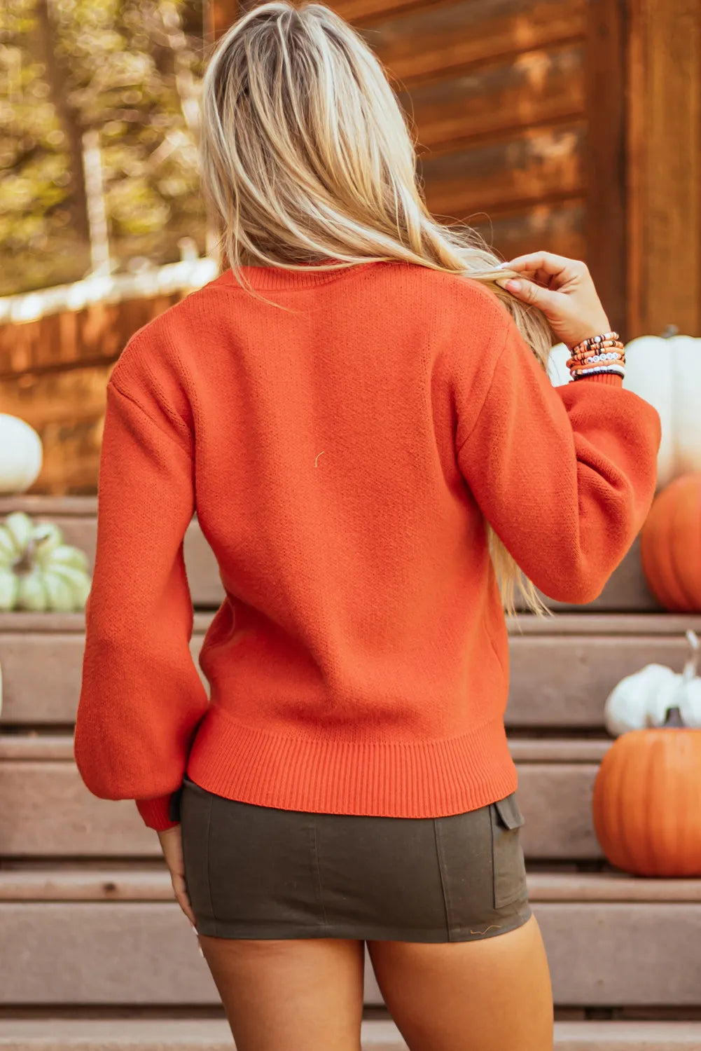 A woman from behind wears an orange pumpkin pattern round neck sweater.