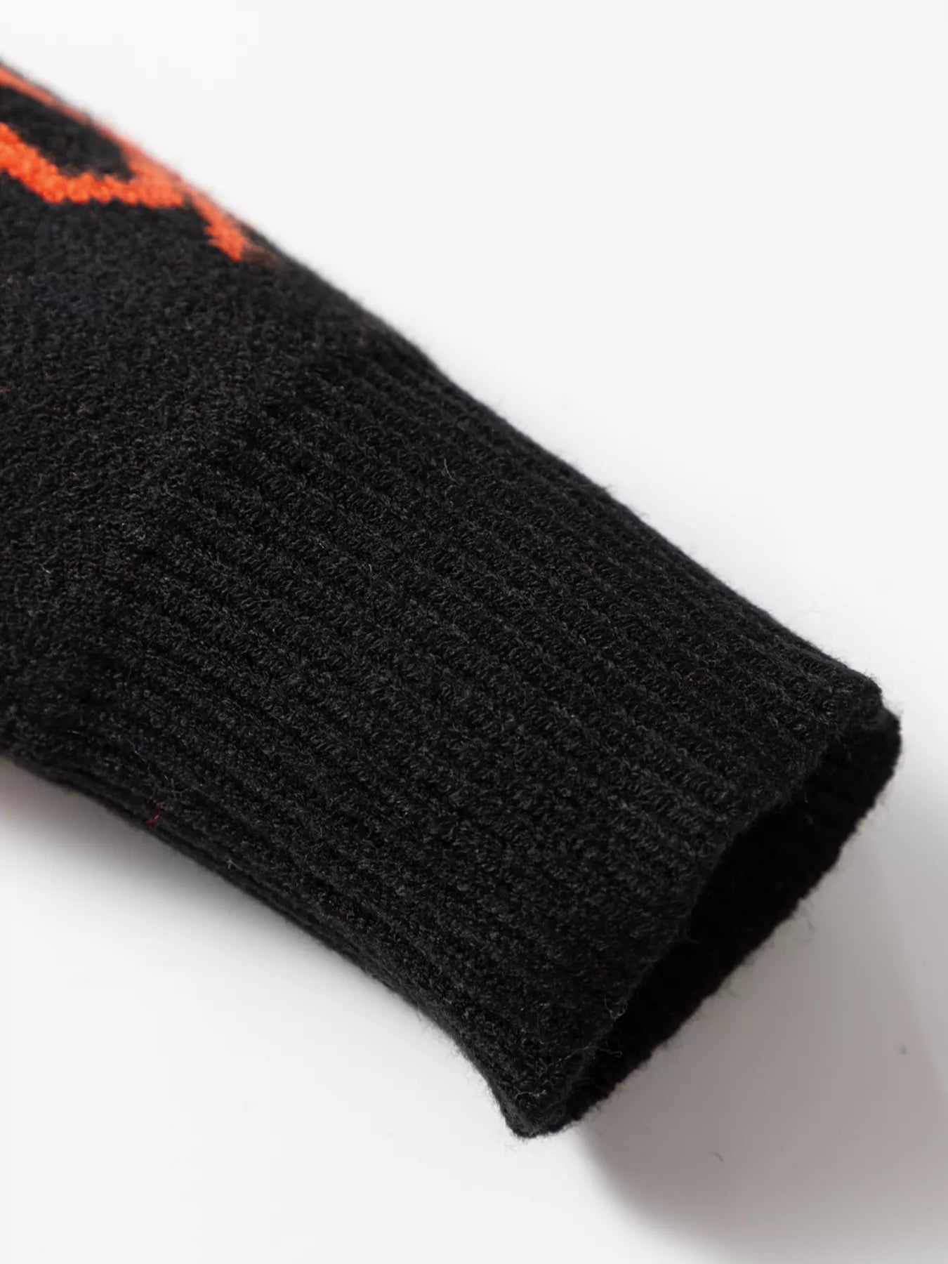 Close-up of a black cardigan sleeve with an orange pumpkin pattern and ribbed cuff.
