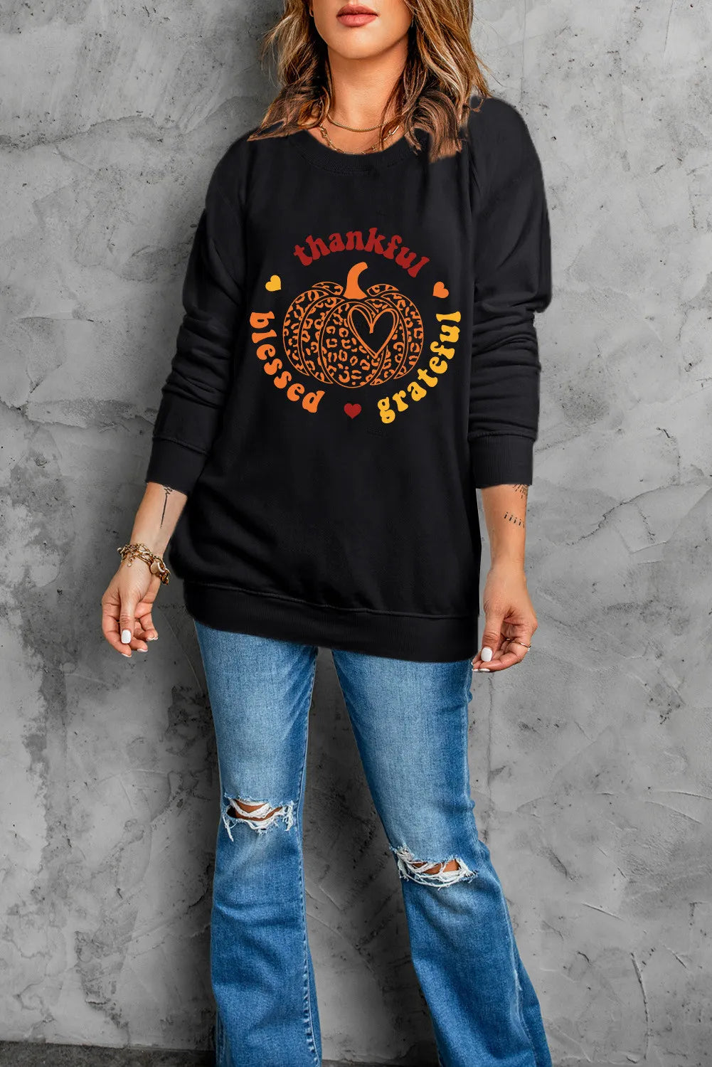 A woman wears a black long-sleeve sweatshirt with a "thankful blessed grateful" pumpkin graphic.
