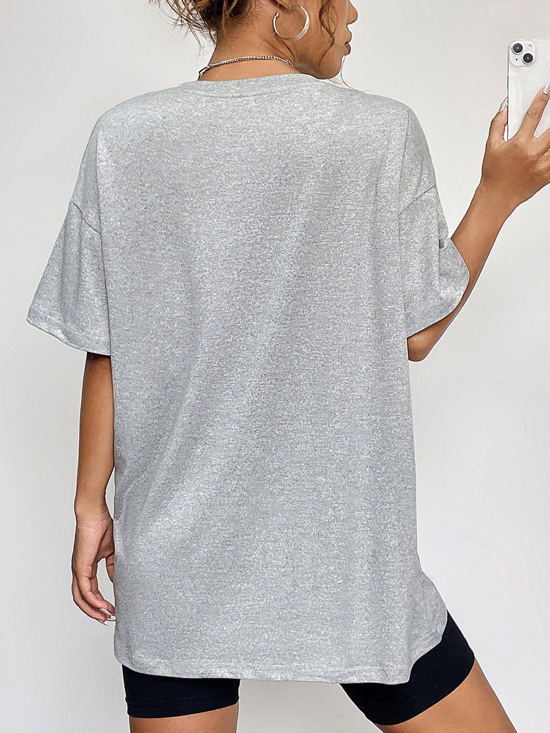 A woman from behind wears a gray round neck short sleeve t-shirt and black shorts.