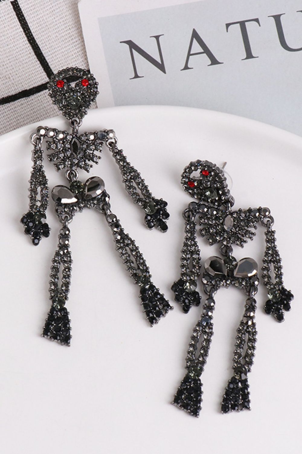 Skeleton-shaped dangle earrings adorned with dark glass stones and red eyes.
