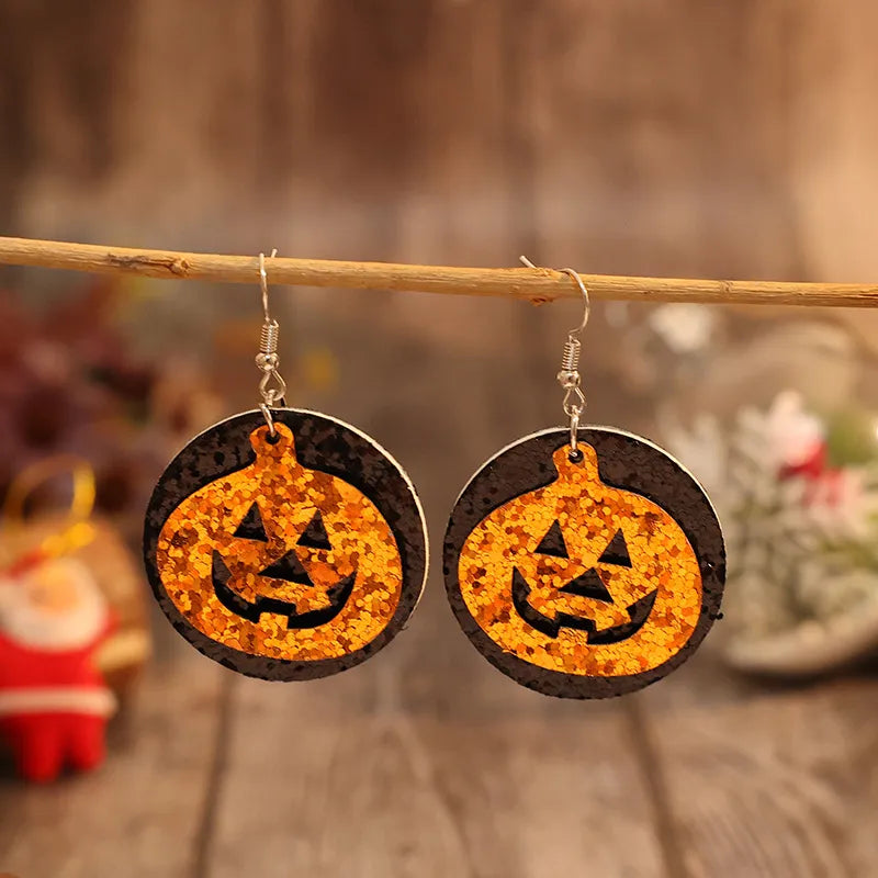 A pair of orange glitter pumpkin earrings with black circular backings hangs from a branch.