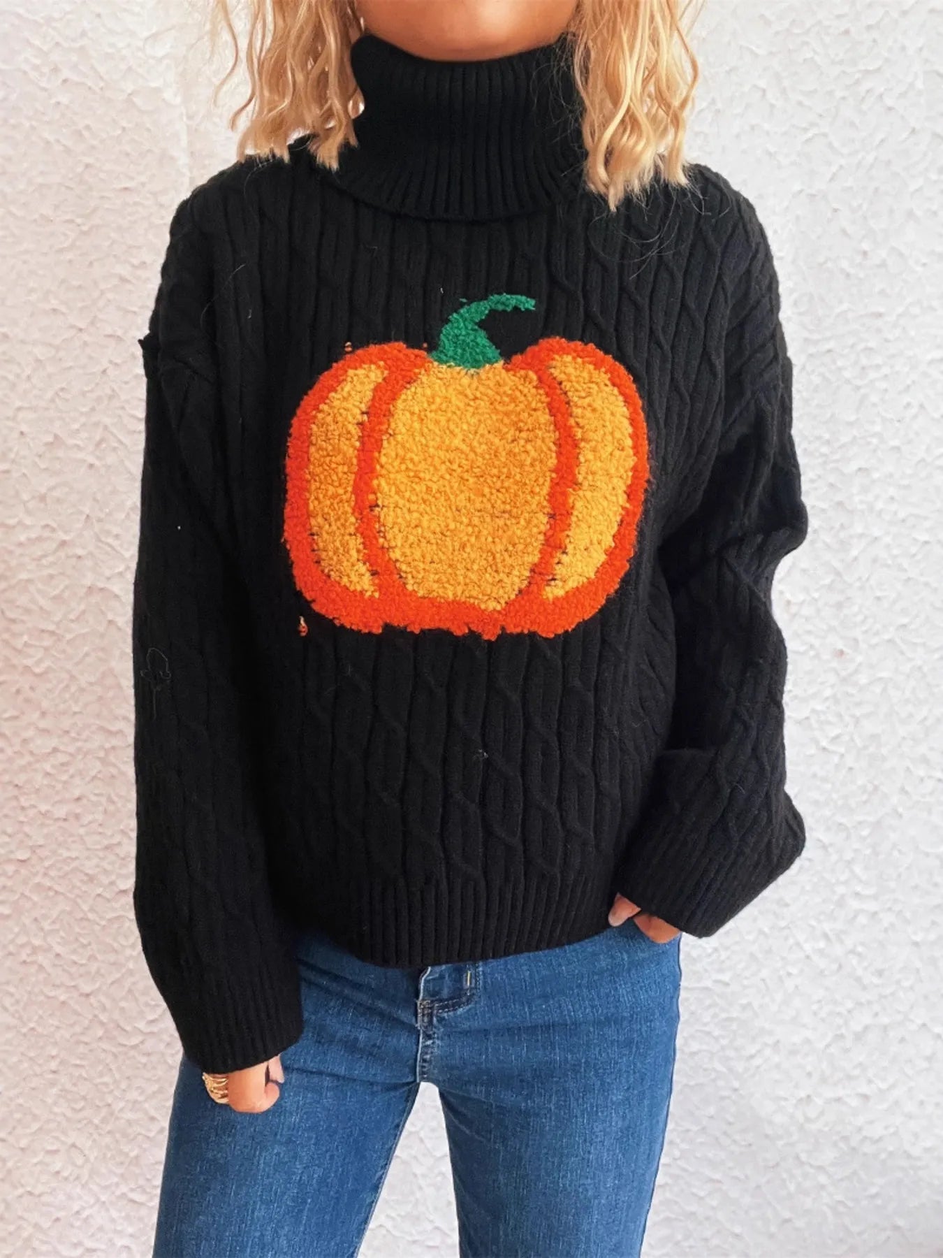 Black cable-knit turtleneck sweater with an orange pumpkin applique.