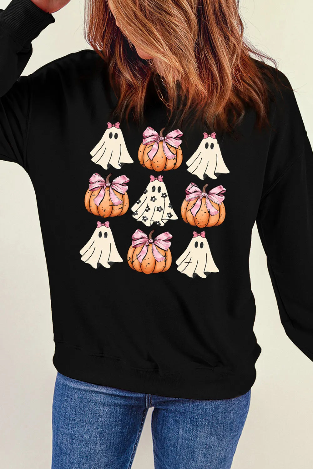 A woman wears a black sweatshirt with a pumpkin and ghost pattern.